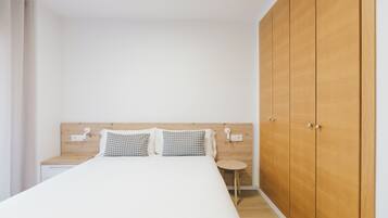 Quarto com guarda-roupa de madeira, cama com almofadas estampadas, mesa de cabeceira e uma pequena mesa redonda.