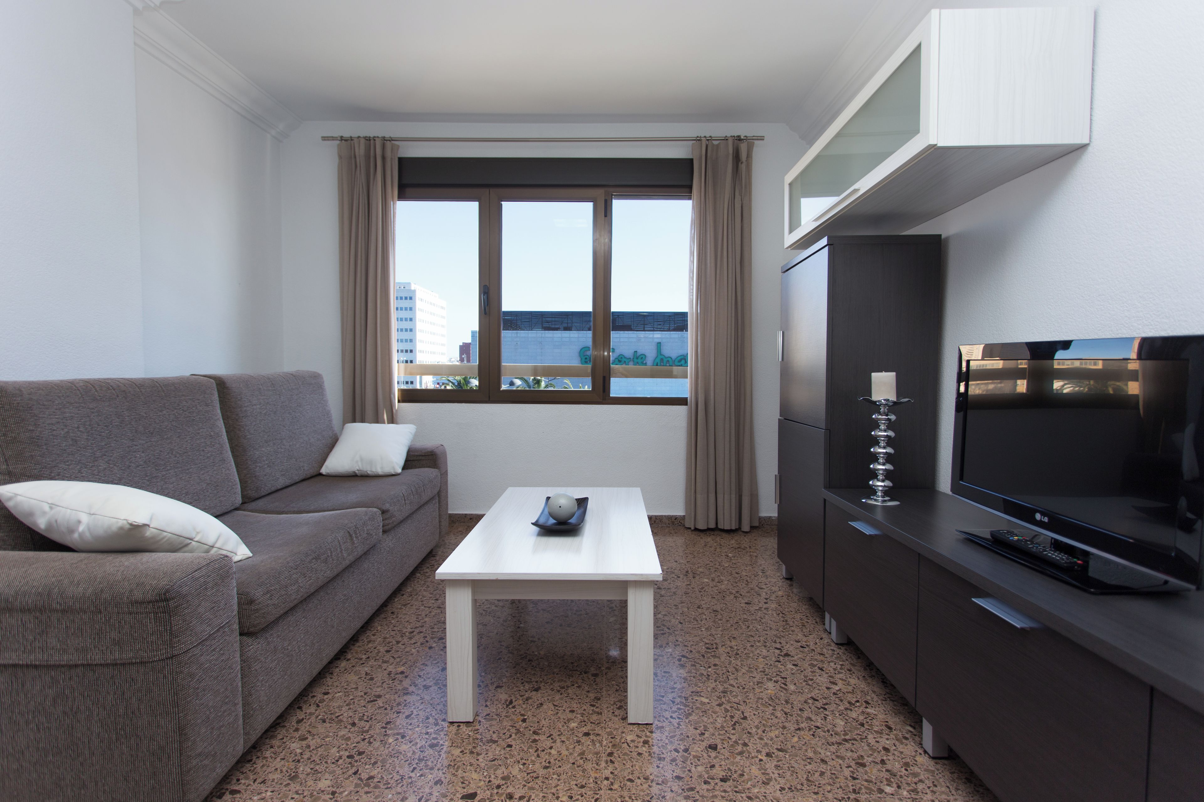 A modern hotel room with a sofa, a small table, a TV, and a view of the city.