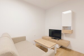 A minimalist living room with a sofa, a TV on a wooden stand, and a small table. - Monlar Campanar (Valencia)