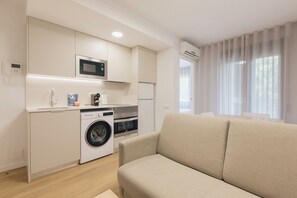 A compact living space with a kitchenette, washing machine, and a sofa. - Monlar Campanar (Valencia)