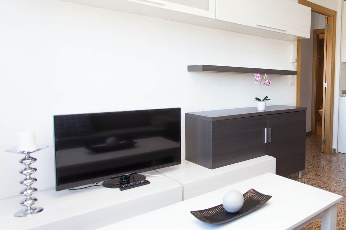 A modern living room with a flat-screen TV, a dark wooden cabinet, a white coffee table, and a small potted plant.
