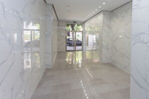 Um corredor com paredes de mármore e chão polido, que leva a uma porta de vidro.