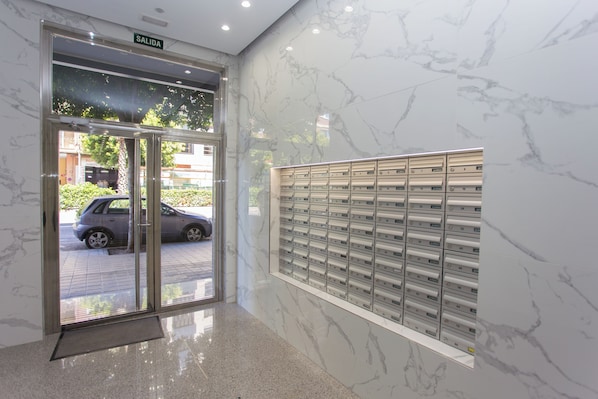 A hotel entrance with a marble wall, a glass door, and a row of mailboxes.