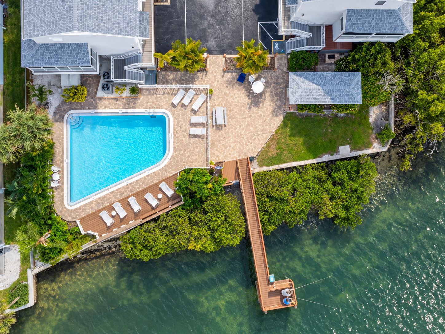 A residential property with a swimming pool, lounge chairs, and a dock extending into the water.