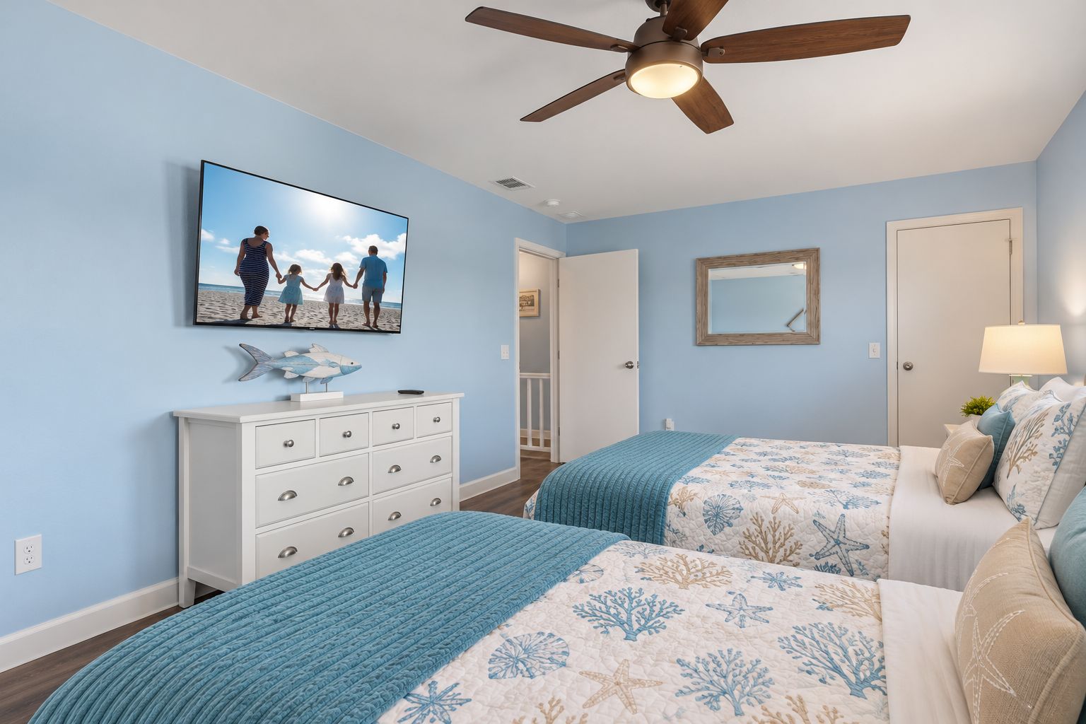 Camera da letto con due letti, una ventola a soffitto, una TV a parete, un comò e una porta che conduce in un'altra stanza.