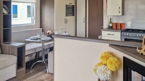 A compact kitchen with a dining area, a built-in TV, and a stove. - Birch 3-bedroom Pet Friendly (Clynderwen)
