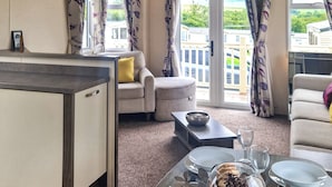 A living room with a sofa, a coffee table, and a dining area with a table set for two. - Birch 3-bedroom Pet Friendly (Clynderwen)