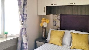 A bedroom with a bed, a nightstand, a vase with flowers, and a window with curtains. - Birch 3-bedroom Pet Friendly (Clynderwen)