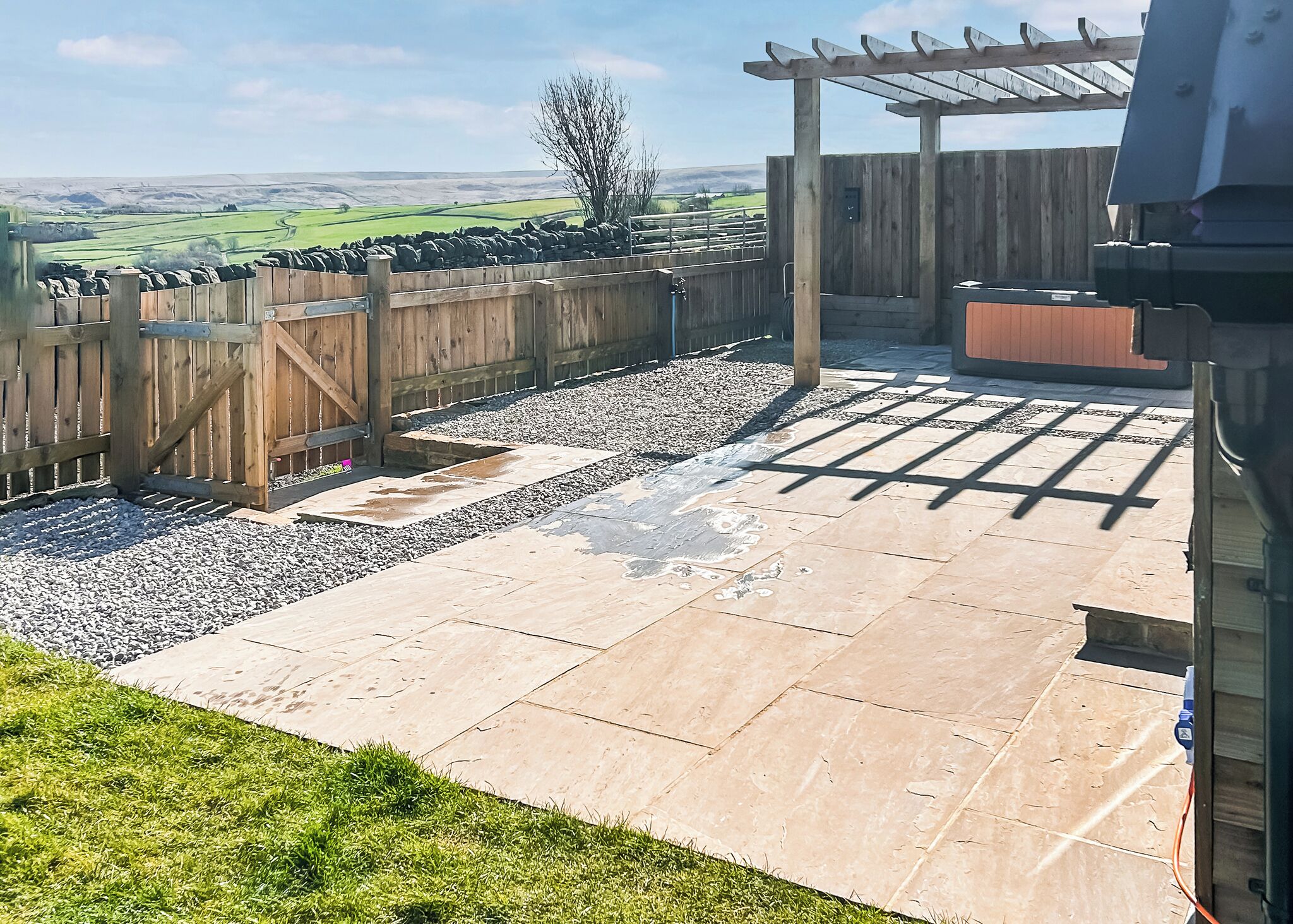 A patio with stone tiles, a wooden fence, and a pergola.