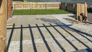 A patio with stone tiles and gravel, a wooden fence, and a dog.