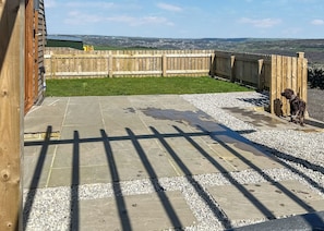 Une terrasse avec des dalles de pierre et du gravier, une clôture en bois et un chien.