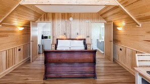 A wooden-paneled room with a bed, bedside tables, and a view into another room.