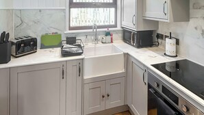 A kitchen with white cabinets, a black stove, a sink, and a window with a view.