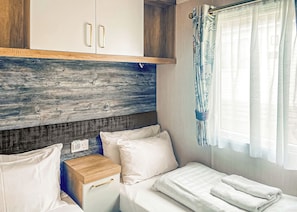 A compact room with a bed, a small bedside table, a wardrobe, and a window with curtains. - Excellent caravan with one double and two twin. (Mortonhall, Edinburgh)