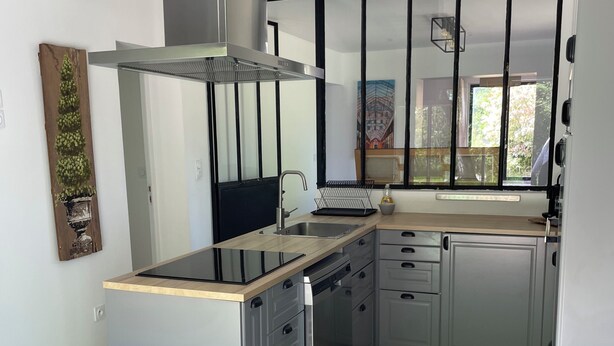A modern kitchen with a central island, stainless steel appliances, and a black-framed window.