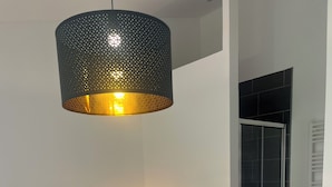 A bedroom with a bed, a bedside lamp, a hanging light fixture, and a sliding glass door leading to a shower area.