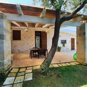 A covered outdoor area with a table and chairs, a tree, and stone walls. - MEST PEPP (Santa Teresa)