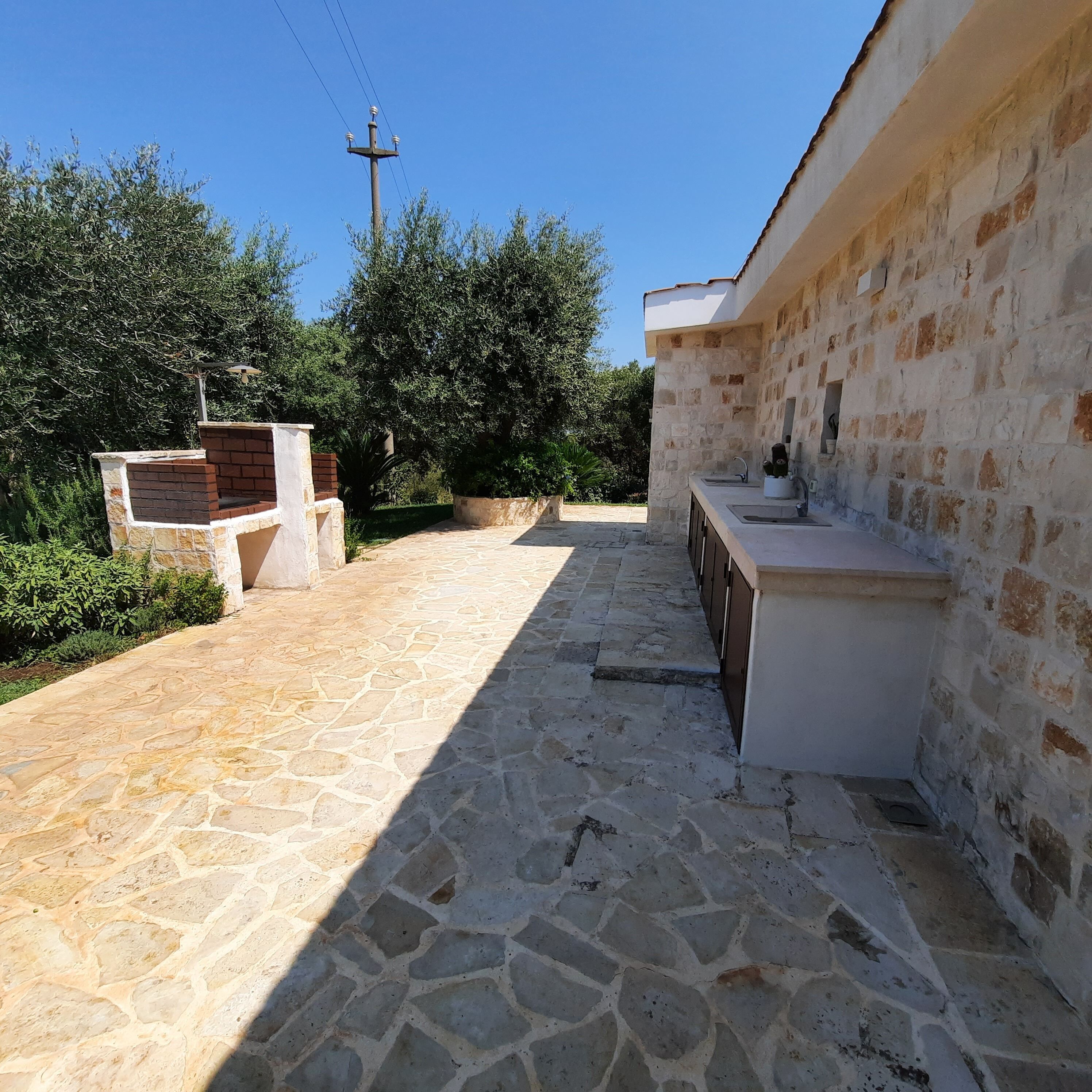 A stone-paved outdoor area with a brick barbecue, stone walls, and a utility pole.