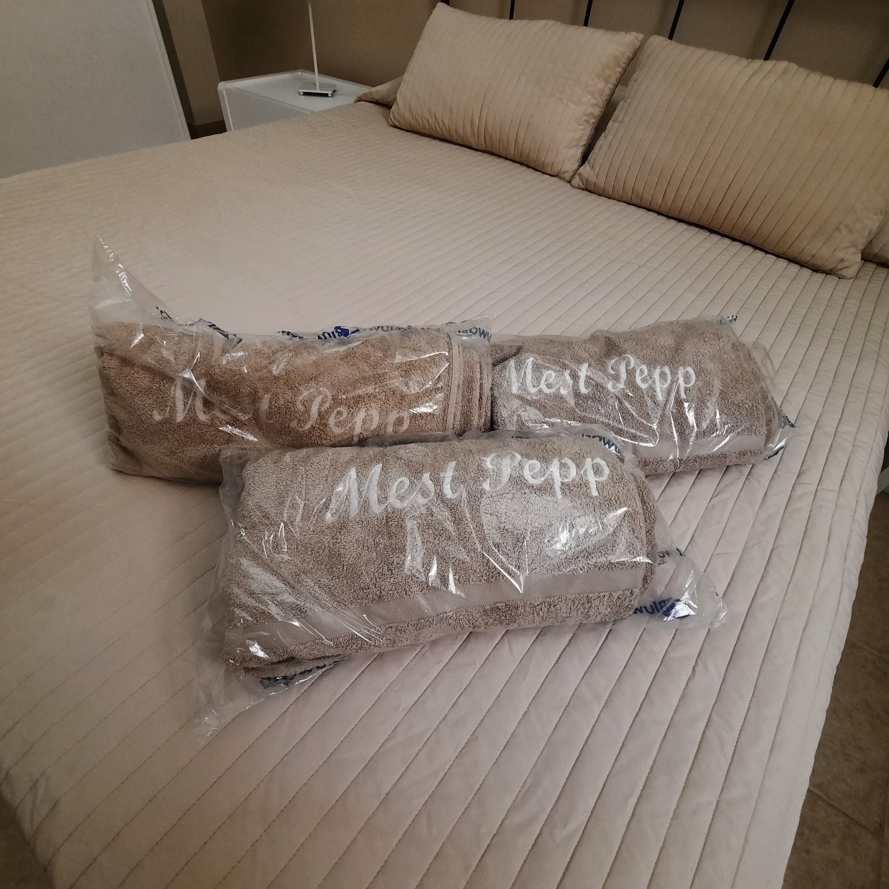 Una cama con cubrecolcha acolchada y tres almohadas envueltas en plástico con el texto 'Mes Reppes'.