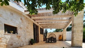 Un edificio de piedra con un patio cubierto, plantas en macetas y una mesa rústica.