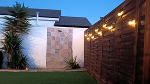 Un jardin avec une pelouse artificielle, une clôture en bois et un mur recouvert de carreaux décoratifs.