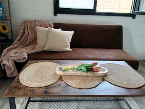 A brown sofa with a woven blanket and pillows, a wooden table with woven placemats and a tray of flowers. - La casita de Pepa, house with garden and a few minutes from the beach of El Palmar. (AN)