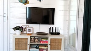 Une pièce avec un mur en bois peint en blanc, un téléviseur fixé au mur, un meuble blanc avec des portes en osier et un plancher en bois.