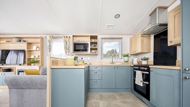 A compact kitchen with a microwave, stove, and cabinets, adjacent to a living area with a sofa and TV. - Platinum 3 Pets allowed Sleeps 6 (Fishguard, Pembrokeshire)