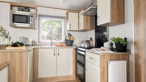 A compact kitchen with wooden cabinets, a microwave, a stove, and a sink. - Platinum 3 Pets allowed Sleeps 6 (Fishguard, Pembrokeshire)