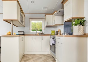 Cocina compacta con armarios blancos, encimera de madera, ventana con persianas y una planta en maceta.