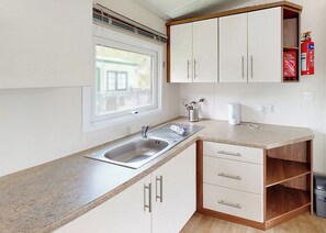Una cucina con lavello, pensili, una finestra e un estintore.