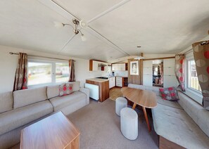 Interni compatti di un camper, con angolo cottura, zona pranzo e salottino con divano e poggiapiedi.