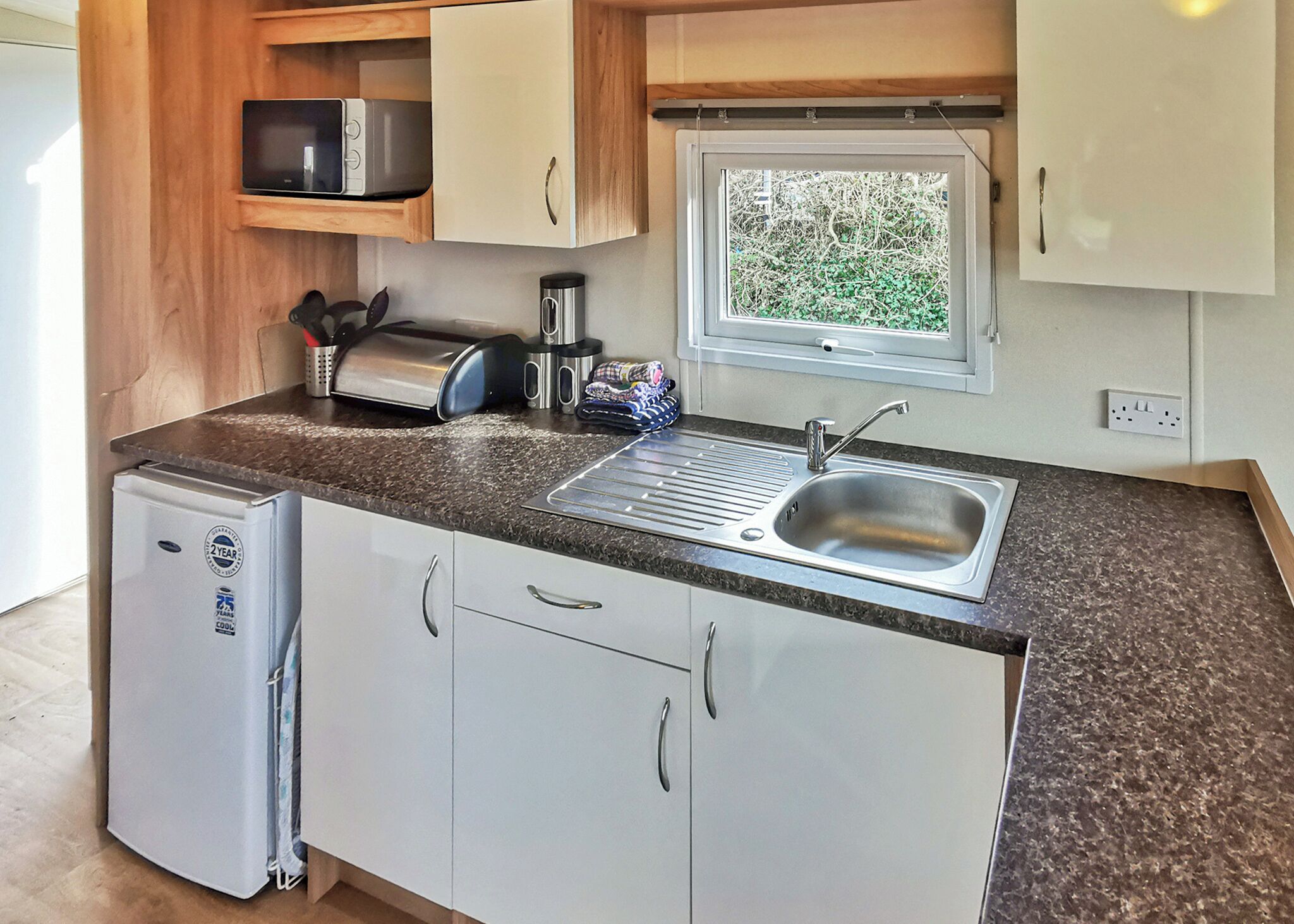 Una kitchenette compacta con lavamanos, microondas, tostadora y refrigerador pequeño.