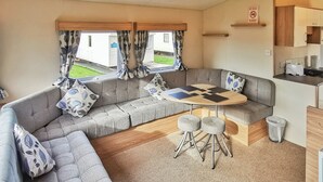 Ein Caravan-Innenraum mit einer Sofagarnitur, einem runden Tisch und einer Küchenzeile.