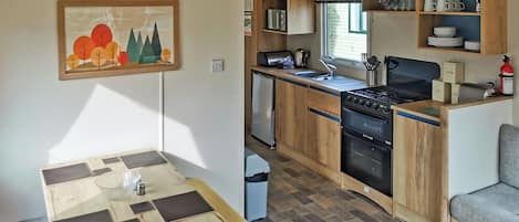 A compact kitchen with wooden cabinets, a stove, a sink, and a dining area with a table and bench.