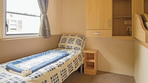 Ein kleines Schlafzimmer mit einem Einzelbett, einem Holzschrank, einer kleinen Ablagefläche und einem Fenster mit Vorhängen.