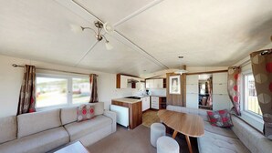 Ein kompaktes Wohnmobil-Interieur mit einer Küchenzeile, einem Essbereich und einer Sitzecke inklusive Sofa und Poufs.