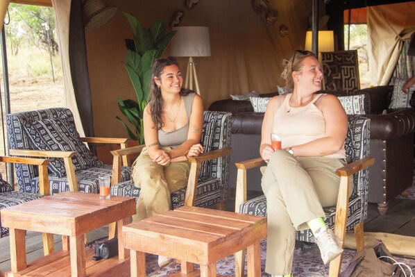 Two people seated on patterned chairs in a room with a wooden table and a lamp. - Africa Safari Serengeti Kogatende (Serengeti)