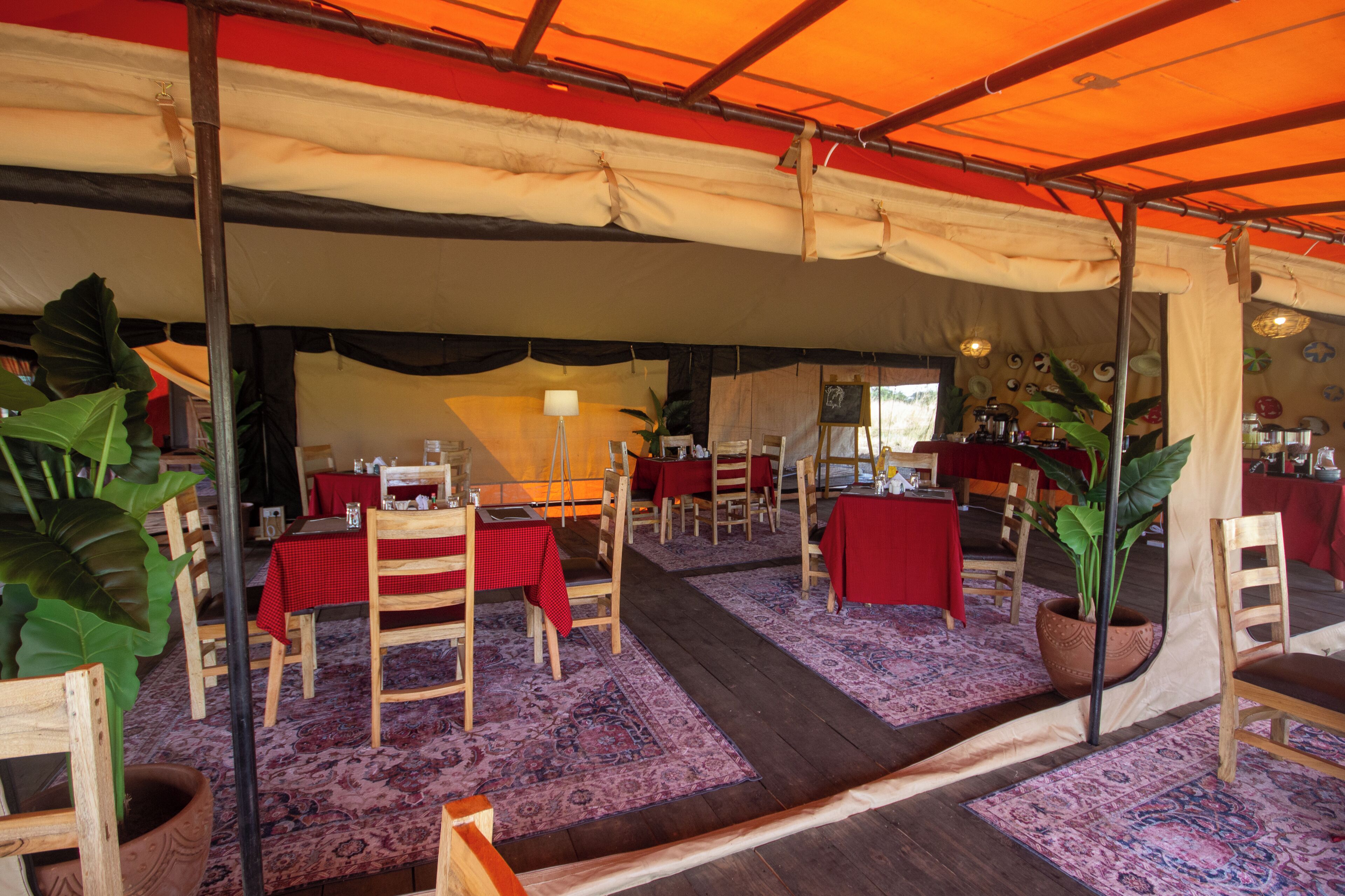 Un área de comedor con carpas, mesas, sillas, una pizarra y plantas en macetas.