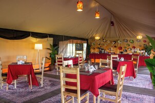 A tented dining area with wooden chairs and tables, red checkered tablecloths, and a variety of wall decorations.