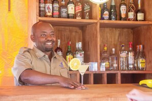 Un cantinero detrás de la barra, con una variedad de botellas de licor al fondo.