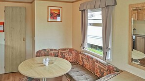 Ein gemütlicher Wohnraum mit rundem Tisch, gepolstertem Sitzplatz, einer Tür, einem Fenster mit Vorhängen und einem gerahmten Bild an der Wand.