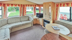 Ein Caravan-Innenraum mit einer Couch, einem Fernseher, einem Tisch und einem Kamin.