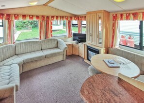 A caravan interior with a sofa, a TV, a table, and a fireplace. - Bronze Plus 3 Bed Pets Sleeps 6 (Clarach Bay, Nr Aberystwyth)