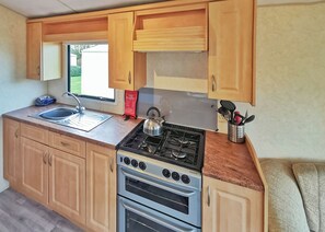 A compact kitchen with wooden cabinets, a gas stove, a sink, and a window. - Bronze Plus 3 Bed Pets Sleeps 6 (Clarach Bay, Nr Aberystwyth)