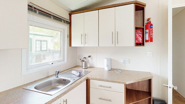 A kitchen with a sink, countertop, cabinets, a window, and a fire extinguisher. - Gold Plus 2 Bed Pet Hot Tub Sleeps 4 (Clarach Bay, Nr Aberystwyth)