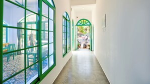 Un pasillo con amplias ventanas arqueadas, suelo de baldosas y vistas a un espacio exterior con mesas y sillas.