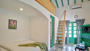 Un dormitorio con cama, una puerta verde, una escalera, un televisor y una mesa con botellas.
