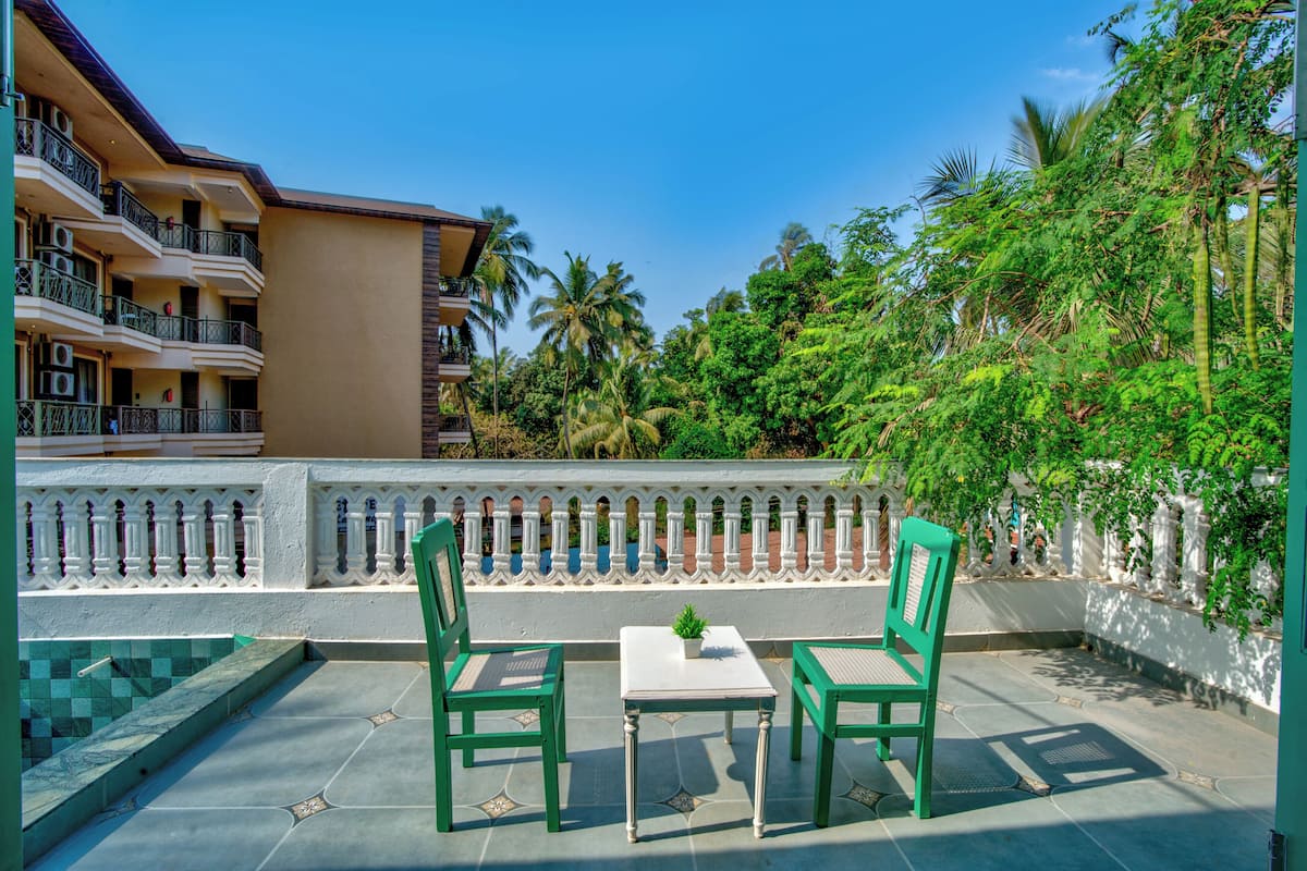 A terrace with two green chairs and a table, a white railing, and a view of a building with balconies and palm trees.