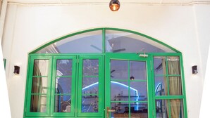 Puerta de vidrio con marco verde, balcón superior, ventilador de techo e iluminación colgante.